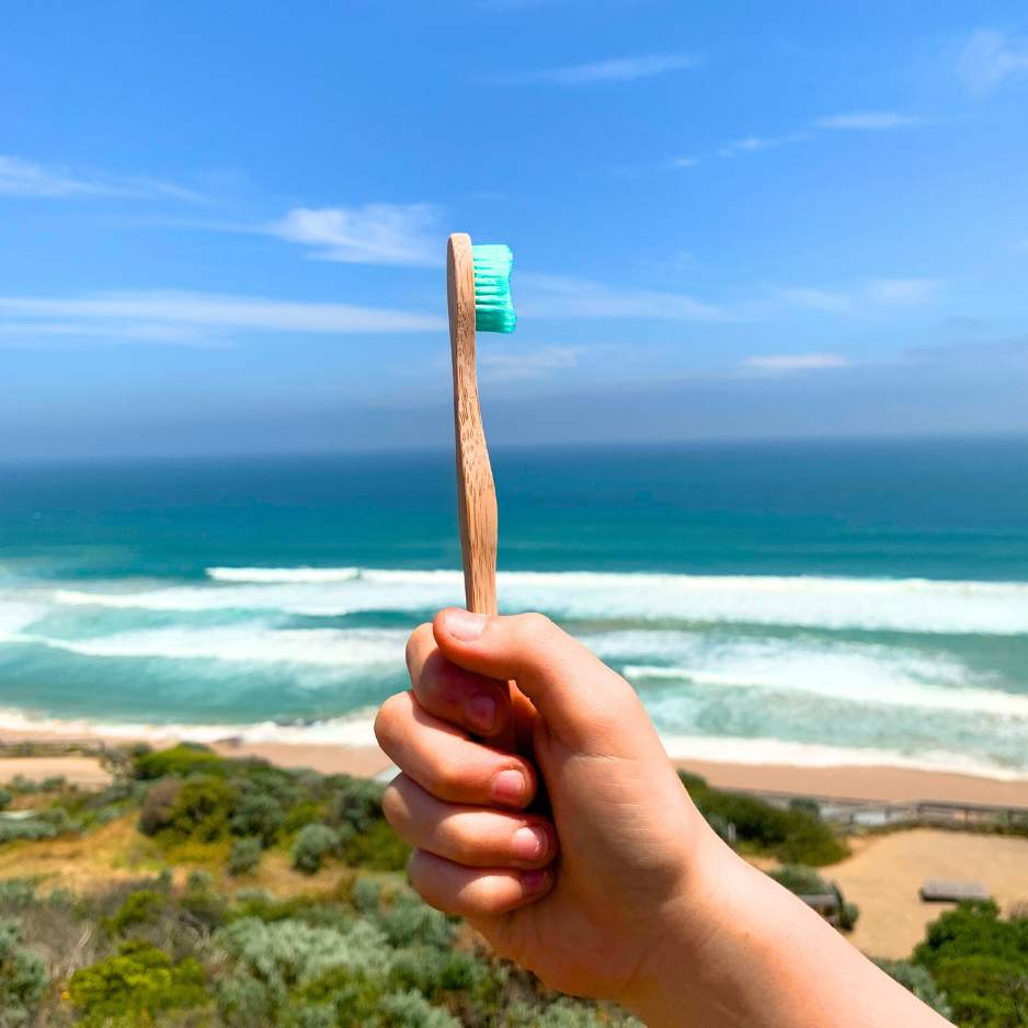Holding a Bamkiki toothbrush as an eco friendly biodegradable sustainable bamboo toothbrush with the ocean and beach background
