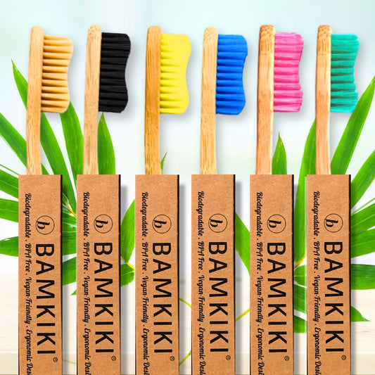 Set of BAMKIKI bamboo toothbrushes with colorful bristle covers on a green leaf background.