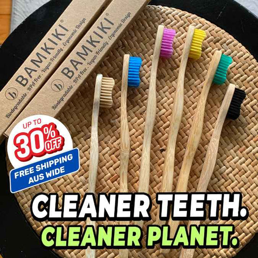 Five bamboo toothbrushes with colorful bristles in blue, pink, yellow, green, teal, and black are arranged on a woven round mat, with two BAMKIKI toothbrush boxes behind them and a promotional badge reading 'UP TO 30% OFF FREE SHIPPING AUS WIDE' and large text 'CLEANER TEETH. CLEANER PLANET.